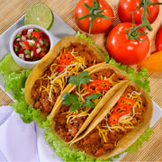 Tacos made with Chata Chicken Taco, served on a plate and accompanied by lettuce, tomatoes, lime, and bell peppers.